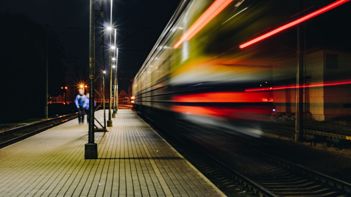 A train blurs past a city transit platform at night in a long exposure